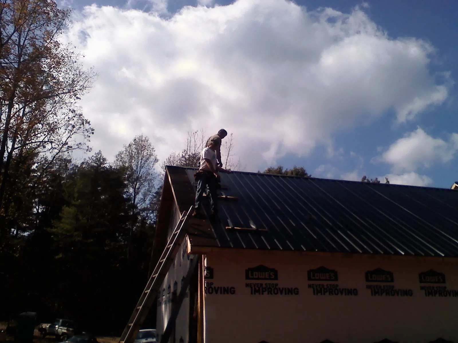 Roofer fastening dark metal panels high against a cloudy sky, from a Roof Inspection job in Columbia